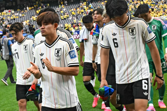 Takefusa Kubo, left, and Shuto Machino walk in front of other teammates on the field, looking defeated