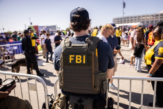 An FBI agent stands near a security point outside behind metal barriers