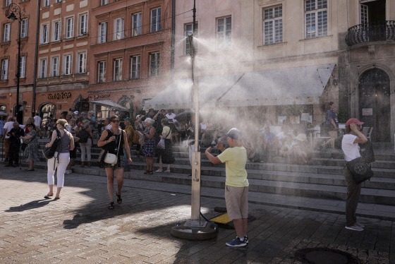 A boy stands in mist from a sprinkler in a brick courtyard.