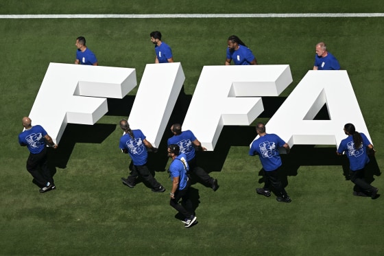 10 men in blue t-shirts carrying giant white letters spelling FIFA