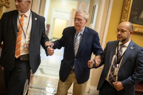 Mitch McConnell holds onto two people's arms for support while walking at the Capitol.