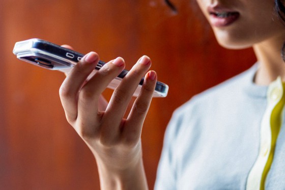 Young woman holds a smartphone to speak a voice message, focused expression and warm indoor lighting.