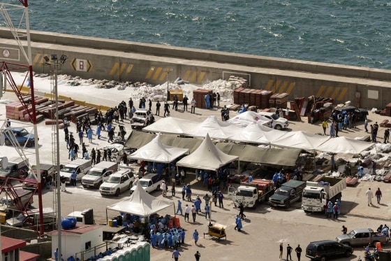 Body bags and coffins laid out on the cement of a seaside pier.