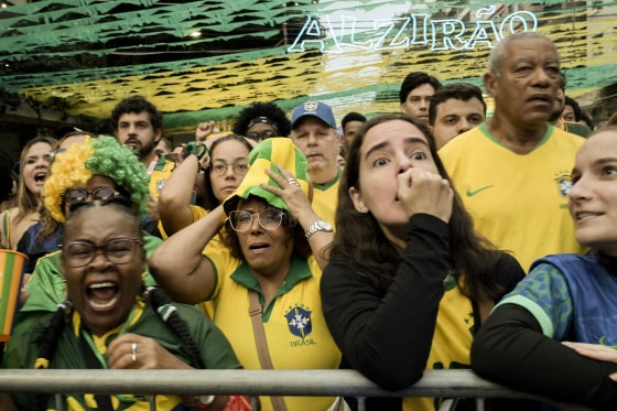 A group of soccer fans wearing the colors of Brazil's team reacting with dismay.
