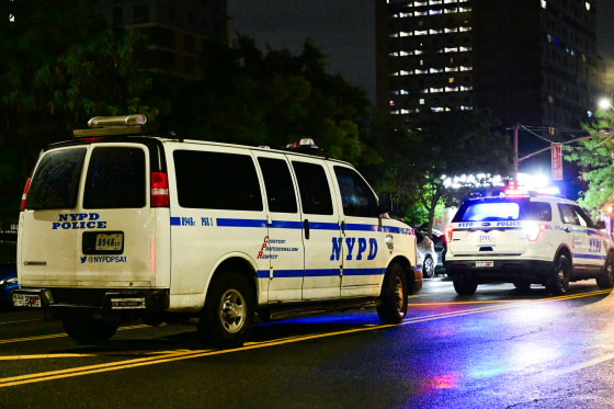 Two NYPD cars drive on the street at night