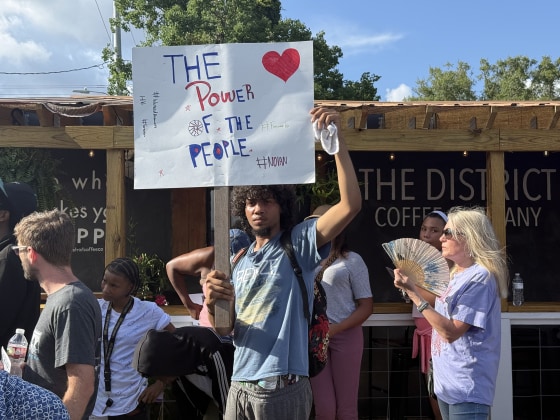 A young man holding a sign reading THE POWER OF THE PEOPLE at a small protest. 