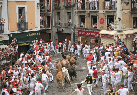 People dressed in white with red neckerchiefs run from bulls on the brick streets of Pamplona.