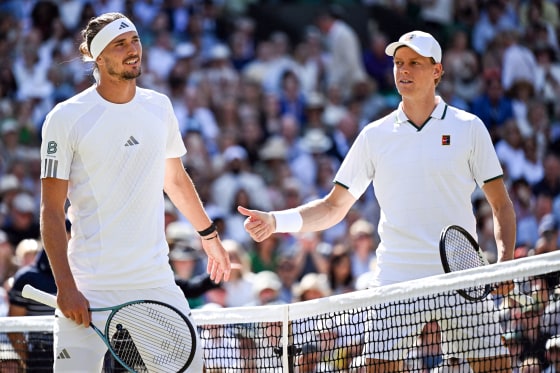 From left, Alexander Zverev and Jannik Sinner stand next to each other on opposite sides of the tennis net between them on the tennis court