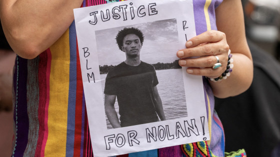 A woman holds a white sign reading JUSTICE FOR NOLAN.
