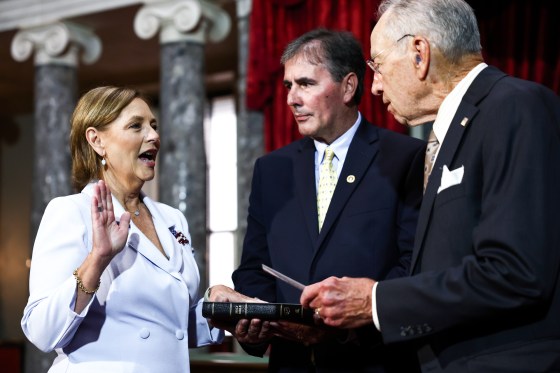 Darline Graham Nordone places her hand on a bible and raises the other as she's sworn in, her husband stands next to her, and Chuck Grassley holds the bible as well standing across from her