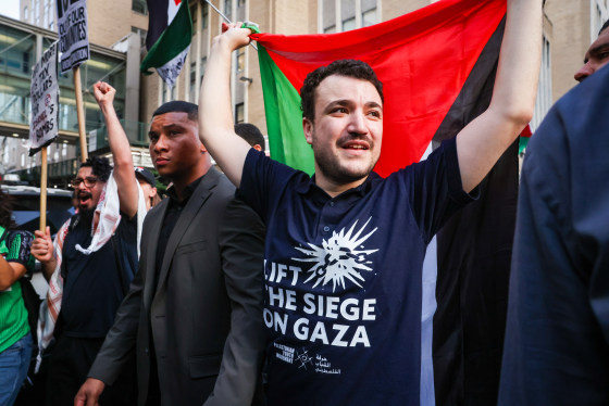 Mahmoud Khalil hold a Palestinian flag behind his back and wears a black shirt with white text on the front that reads "Lift the siege on Gaza"