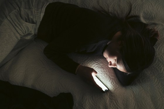 Image: Directly above shot young woman text messaging on smart phone while lying on bed in bedroom at night