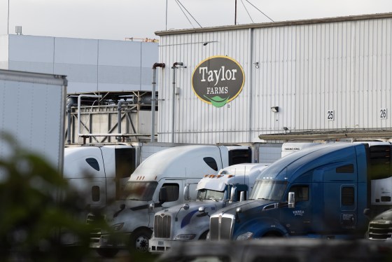 Several semi-trucks parked in front of a warehouse with the Taylor Farms logo on its facade.