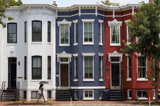 A woman with an umbrella walks past red, white and blue painted row houses.