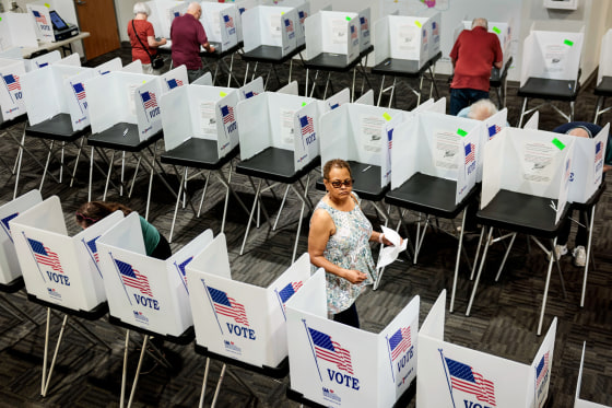 Pamela Dear walks down an aisle between rows of voting booths inside of a room