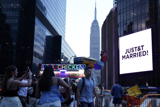 A giant screen on the side of Madison Square Garden as people take photos; the Empire State Building in the background.
