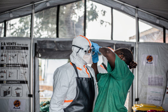 A hygiene worker helps a doctor put on personal protective equipment inside of a room