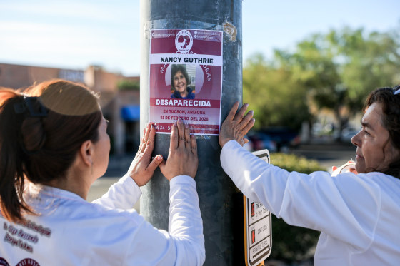 Raquel Navarro, left, and Lupita Tello, place a flyer that reads, 'Nancy Guthrie Desparecida' (Disappeared) on a pole outside