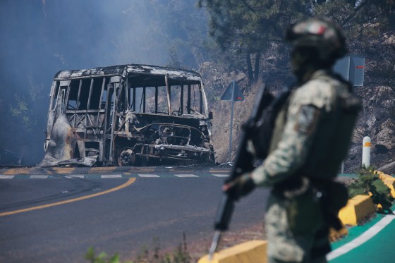 A soldier stands guard by a charred vehicle.