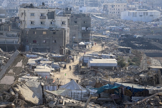 A high-angle view shows makeshift shelters and tents among damaged buildings and rubble.