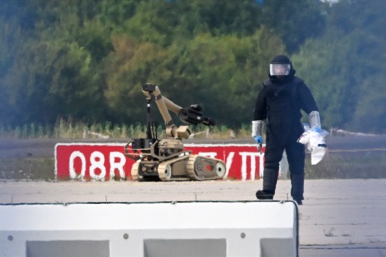 A forensic technician works alongside a bomb-disposal robot.