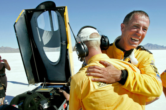Andy Green, right, is hugged by a crew member next to a vehice with it's hood open outside