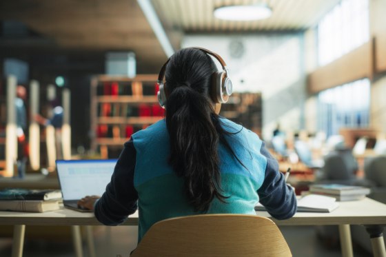 Image: Female student wearing headphones while working on laptop in a public library.