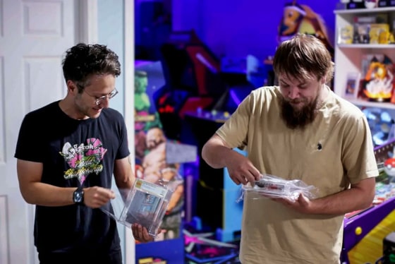 Two men stand while holding video games cases on their hands.
