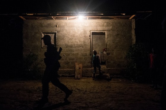 A guerrilla member walks in front of a house as a child appears to walk-in.
