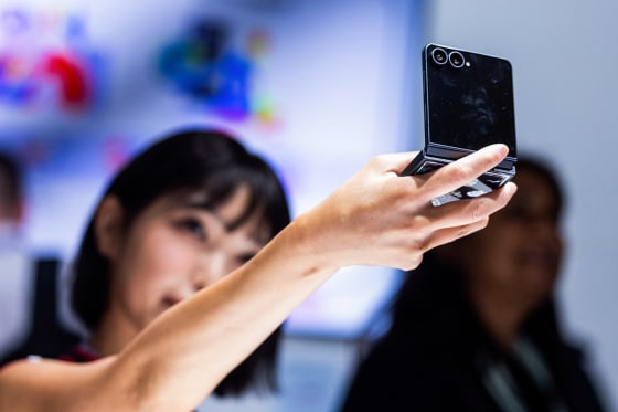 A woman holds a Samsung Galaxy Z Flip 8 up into the air while looking into it