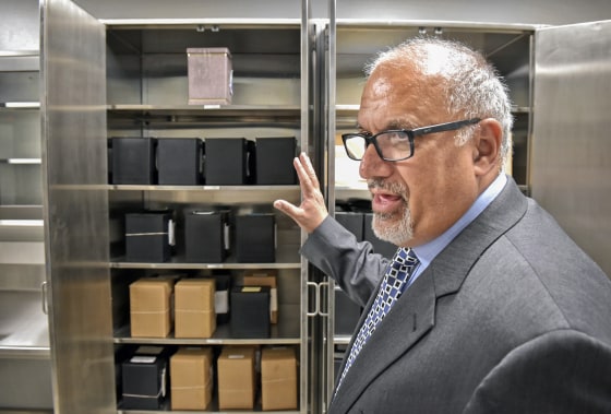 Stephen Diamantoni gestures toward an open filing cabinet filled with black boxes of cremated remains.