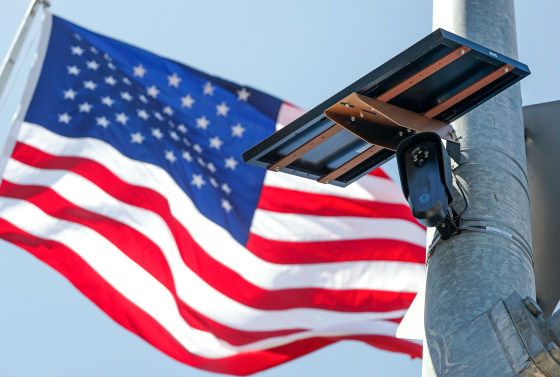 An American flag flies behind a Flock Safety camera tmounted to a light pole