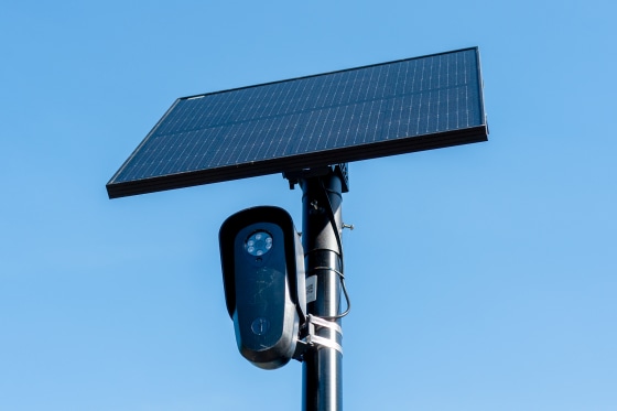 A Flock camera is mounted on a pole underneath a solar power panel
