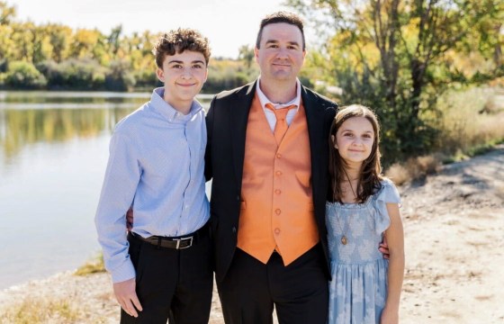 A portrait of a father and two children dressed in formal wear on the banks of a river.
