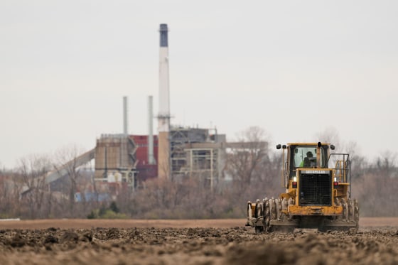 A worker prepares a plot of land for an AI data center in Independence, Mo., on March 24, 2026. A retired power plant in the background is being refurbished to provide electricity for the facility.