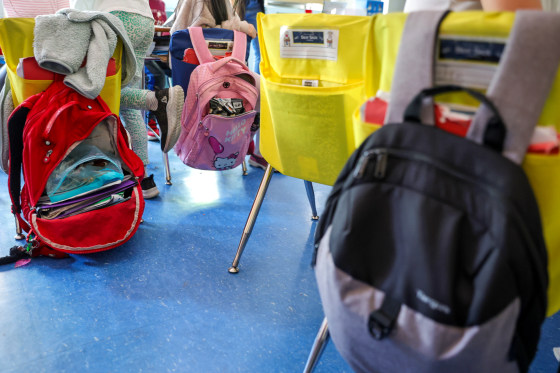 Student backpacks hang on the backs of classroom chairs.