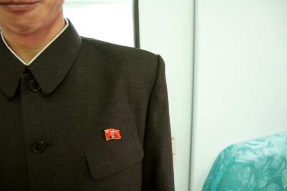 All North Koreans wear a Kim Il-sung pin when out and about. There typically seems to be two types of pins: one with Kim's face on a flag-shaped background and another of Kim's face on a small round button. In the case of our government-appointed minder, he often wears one pin on his suit jacket and another on his white collared shirt.