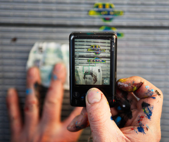 Artist Ben Wilson uses a bank note to provide scale as he takes a photograph of one of his miniature paintings made on discarded chewing gum on the Millennium Bridge, in London February 28, 2012. Wilson has painted miniature works of art on discarded chewing gum in various parts of London and Europe over the past seven years in an effort to