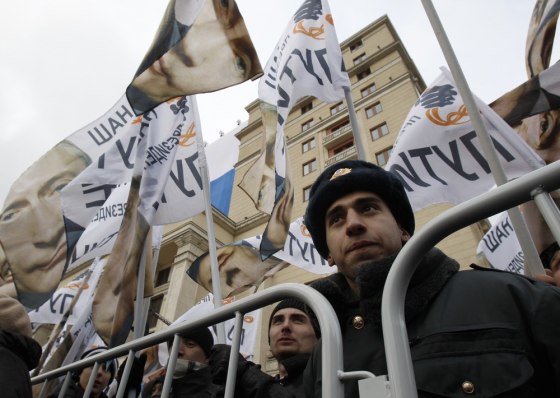 A Russian police officer stands by a barricade as supporters of Russia's Prime Minister Vladimir Putin wave flags during a rally in central Moscow March 5, 2012. International monitors said on Monday Russia's presidential election was clearly skewed to favour Putin, a verdict that could spur protesters planning to take to the streets to challenge his right to rule. REUTERS/Sergei Karpukhin (RUSSIA - Tags: POLITICS ELECTIONS CIVIL UNREST)