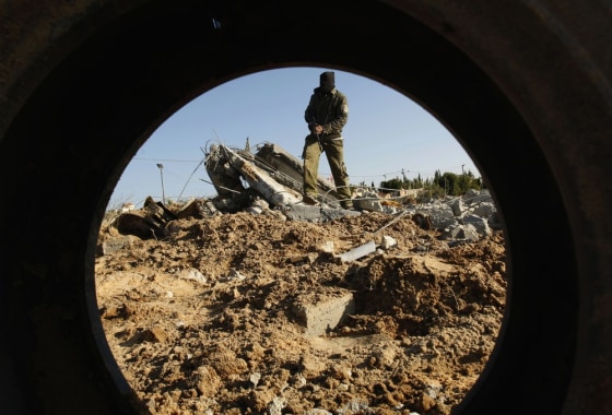 A masked Palestinian Islamic Jihad militant is seen through a tyre as he surveys the damage at a training camp after an Israeli air strike in Gaza December 29, 2011. The Israeli army confirmed that it targeted two sites in Gaza, including the training camp, and added that the strikes were carried out in response to the firing of rockets from Gaza into Israel on Wednesday. No injures were reported in Gaza. REUTERS/Ibraheem Abu Mustafa (GAZA - Tags: POLITICS CIVIL UNREST TPX IMAGES OF THE DAY)