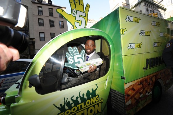 In this photo taken by AP Images for Subway, NY Giants defensive end and world champion Justin Tuck rides in the Footlong Nation vehicle to give fans free $5 Footlongs in celebration of Subway restaurants' FebruANY.