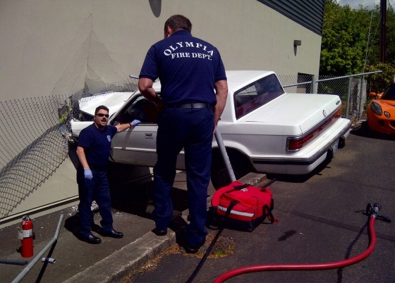 Firefighters discuss how to remove a man from a car after he crashed it into TVW Studios in Olympia, Wash., on Wednesday. The vehicle crashed into the side of the building Wednesday afternoon and was left hanging over an alley. The driver was alert and talking with emergency responders as they worked to figure out a safe way to remove him.