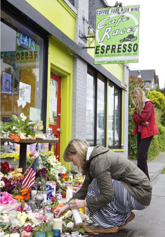 Maggie Ritnour lights a candle at a makeshift memorial at Cafe Racer in north Seattle Thursday as Kara Bazzi looks on.
