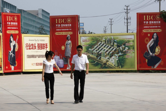 People walk in front of posters advertising International Bag City in Pinghu, Zhejiang province September 28, 2012.
