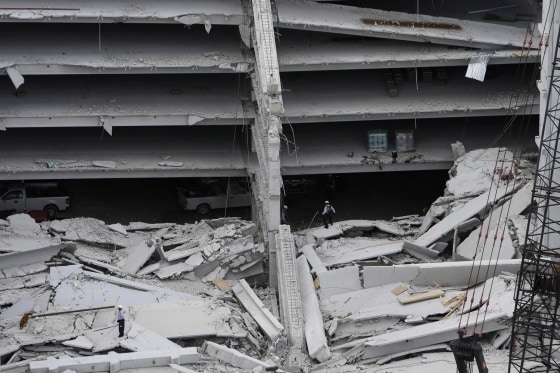 A dog walks through the rubble, lower left, with rescue workers at a five-story parking garage after it collapsed at Miami-Dade College, on Oct. 10, in Miami, killing one worker and trapping two others in the rubble, officials said. Several other workers were hurt, including one rescued from the debris.
