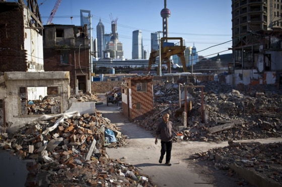 A resident holds a spittoon as he walks in an area where old residential buildings are being demolished to make room for new skyscrapers in central Shanghai on October 17, 2012.