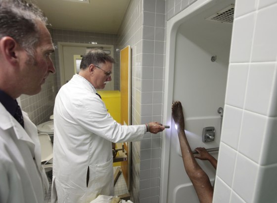 Dr. David Mathis, center, accompanied by physician's assistant Rob Johnson, left, examines a sore on the foot of an inmate at the California Medical Facility in Vacaville, Calif., Sept. 12.