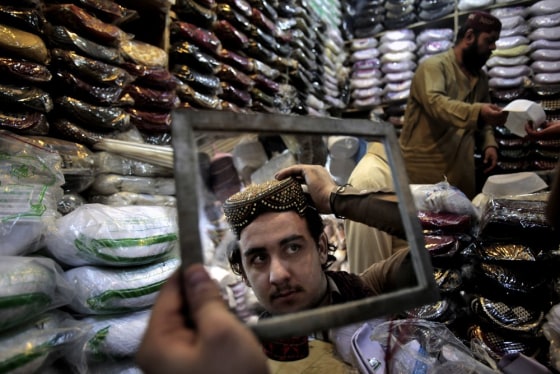 A Pakistani man is reflected in a mirror while trying on a traditional hat, as he and others buy new clothes for the upcoming Muslim holiday of Eid al-Adha in Peshawar, Pakistan on Oct. 24, 2012.