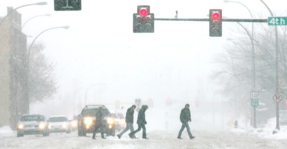 In this photo from Sunday, pedestrians cross snow-covered Main Avenue in downtown Fargo, N.D.