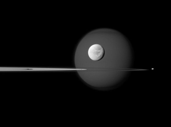 Four moons of Saturn are visible in this image from the Cassini orbiter: Bright Dione is in the foreground, with Titan in the background. The dot just to the right of Saturn's nearly edge-on rings is Pandora, and Pan is just a speck embedded within the rings, to the left of Titan and Dione.